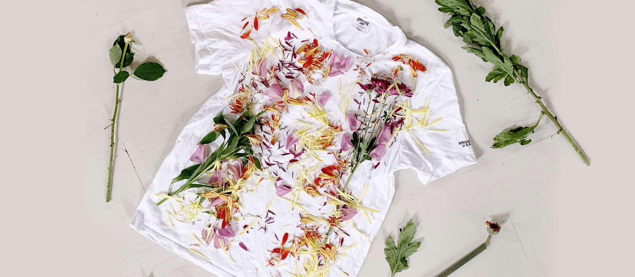 White t-shirt laid out with flowers and greens laying on it. 